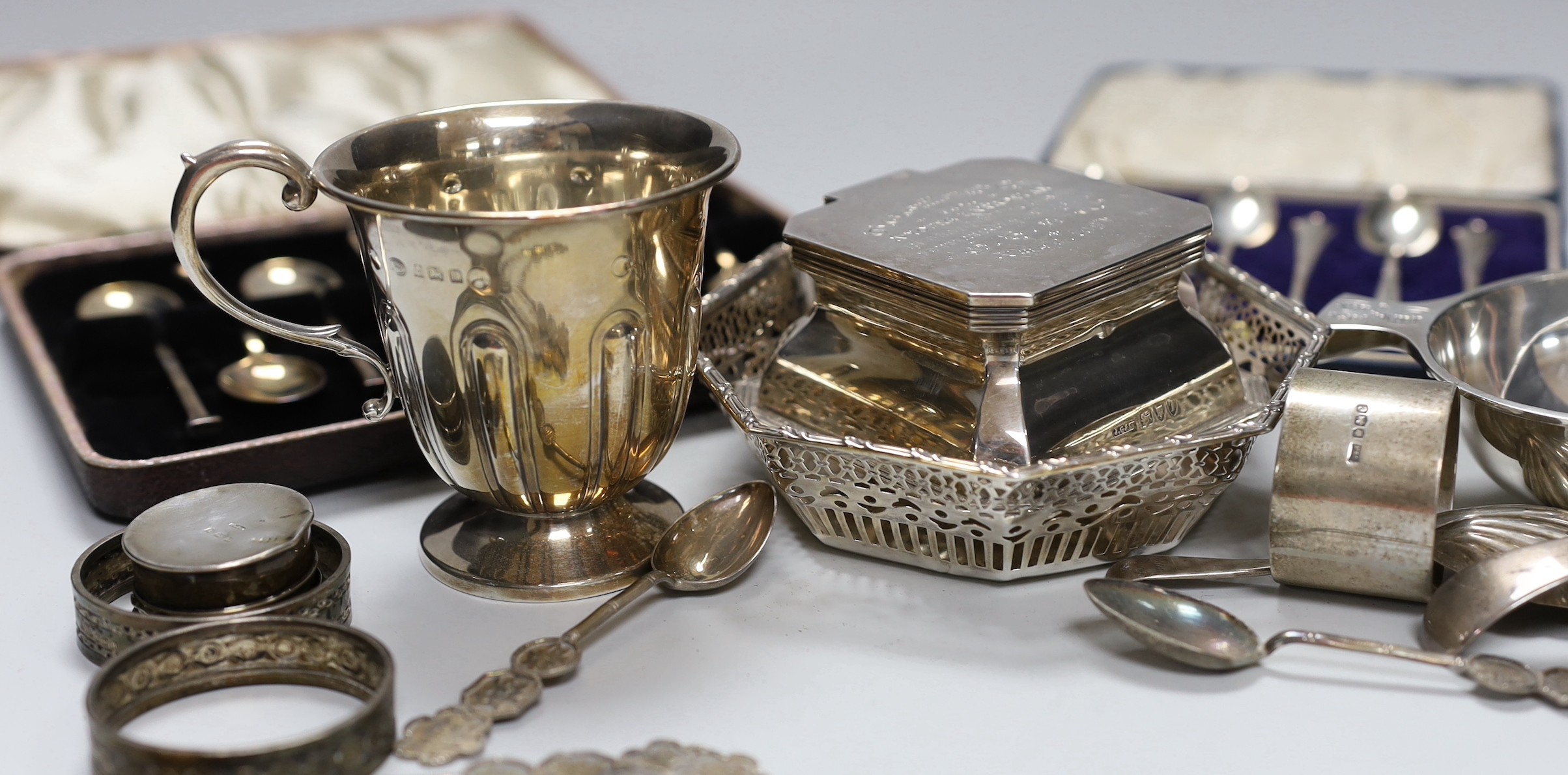 Assorted silver ware including two cased sets of six teaspoons, one with tongs, a christening mug, pierced sterling octagonal bowl, a Scottish silver quaich, inkwell, salt, three napkin rings, enamelled pill box, sifter